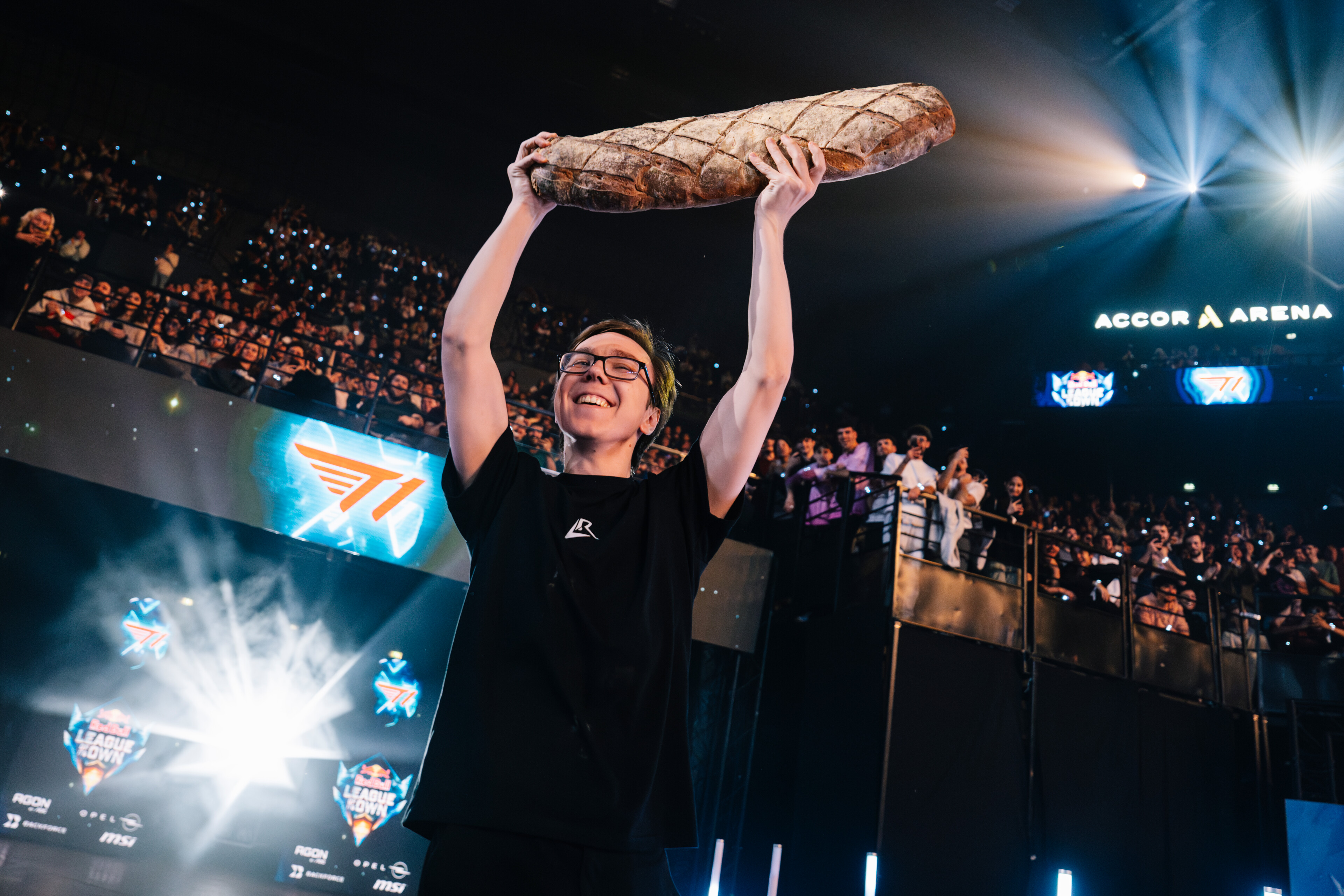 Thebausffs grinning on stage at the Accor Arena in Paris, holding an enormous loaf of bread above his head